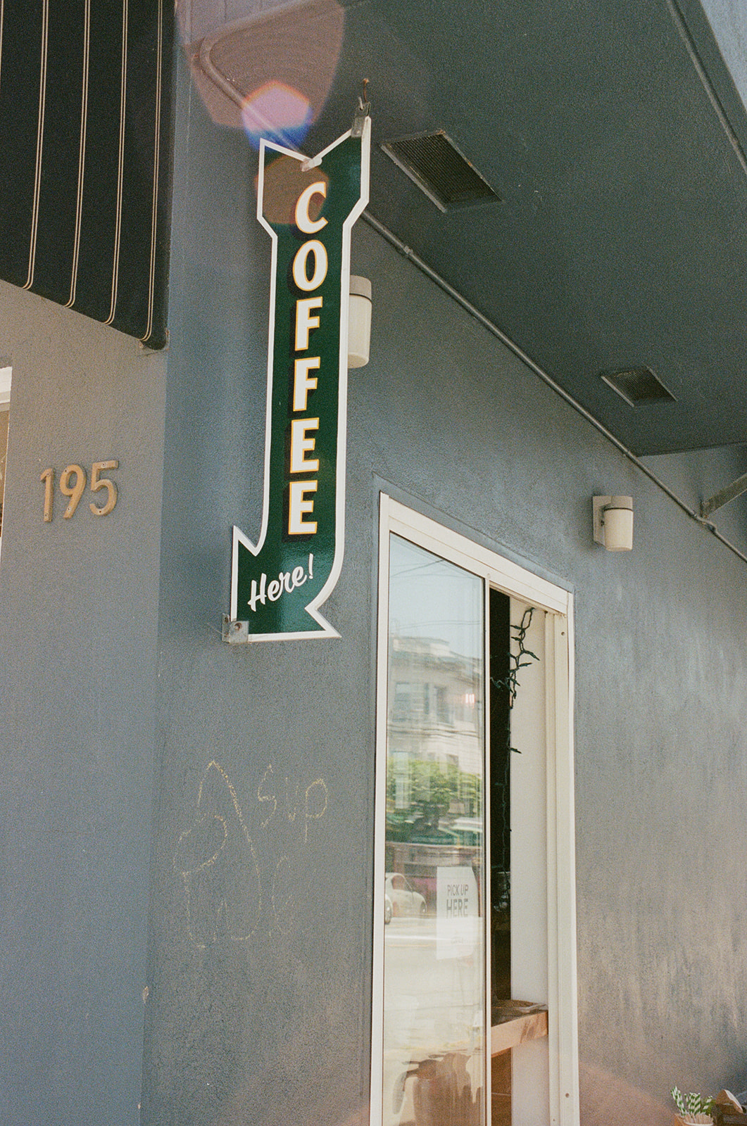 A photograph of a blue building with a green sign shaped like an arrow that says 'Coffee' on it in white text. There's a chalk drawing of an Among Us crewmate on the wall of the building.